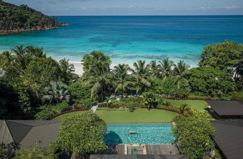 Ocean-view infinity pool and palm trees at Four Seasons Resort Seychelles, taken from a hillside villa under clear skies